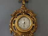 a gold clock hanging on the wall with a bird on it