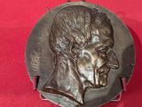 une plaque en bronze représentant le visage d'un homme sur un fond rouge