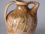 a brown vase with a handle on a gray surface