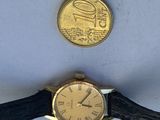 a gold watch sitting next to a coin on a white surface