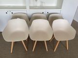 four white chairs with wooden legs in front of a bookcase