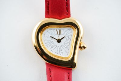 a heart shaped watch on a red strap on a white surface
