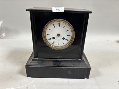une petite horloge noire avec un cadran blanc posée sur une table