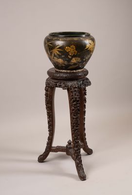 une image représentant un vase noir et doré posé sur un socle en bois