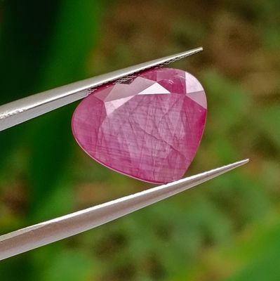 une personne tenant une pince sur laquelle est fixée une pierre rose en forme de cœur