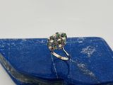 un gros plan d'une bague sertie d'un diamant et d'une émeraude, posée sur une pierre bleue