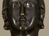 bronze head of a woman with ear rings on a white surface