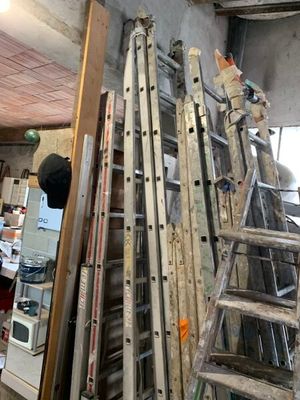 un homme debout sur une échelle dans une pièce où se trouvent de nombreuses échelles