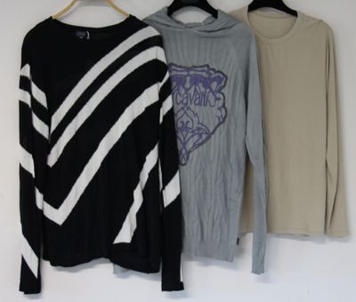 three sweaters hanging on a clothes rack in front of a white wall
