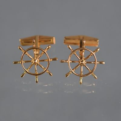 two pairs of gold cufflinks with a ship wheel on them