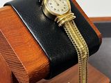 une montre posée sur un socle en bois, attachée à une chaîne en or