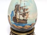 painting of a ship on an egg on a stand on a white surface
