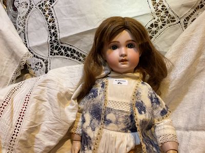 une poupée assise sur un lit avec un ours en peluche