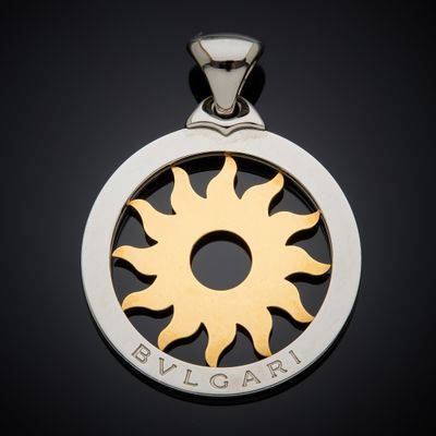a close up of a silver and gold pendant with a sun