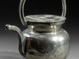 une théière ancienne en argent, dotée d'une anse, posée sur une surface blanche