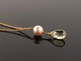 a close up of a necklace with a pearl and a green crystal