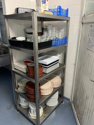 une étagère en métal sur laquelle sont posés des assiettes et des verres, dans une cuisine
