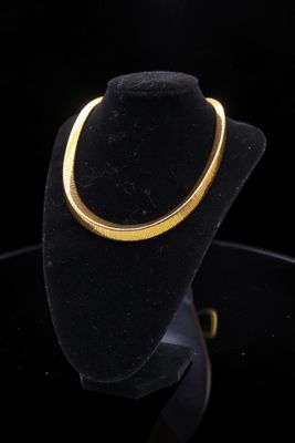 a gold necklace on a black mannequin stand against a black background