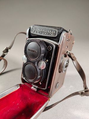 un appareil photo à l'ancienne, dans un étui rouge, posé sur une table