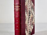 an old red book sitting on top of a table next to a white wall