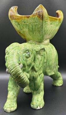 un petit éléphant vert avec un grand bol vert sur le dos