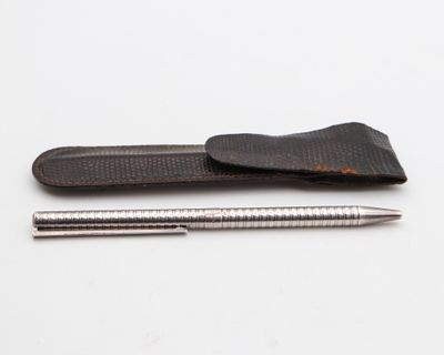 étui en cuir avec un stylo et un crayon posés sur une surface blanche