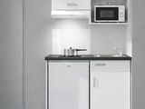 une petite cuisine avec des placards blancs et des plans de travail noirs