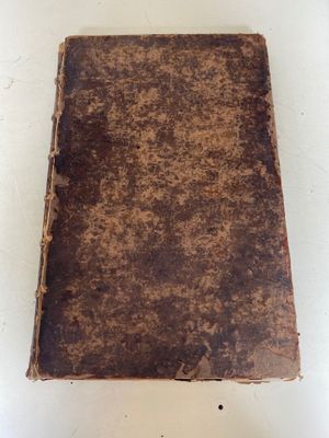 un vieux livre posé sur une table à côté d'un mur blanc