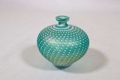 une image représentant un vase vert et blanc posé sur une surface blanche