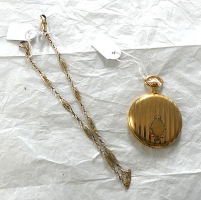 une montre de poche en or et une chaîne en or posées sur un morceau de papier