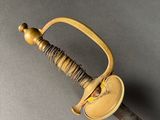 a close up of a sword with a wooden handle on a gray surface