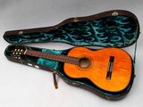 une photo d'une guitare acoustique dans son étui, posée sur une surface blanche