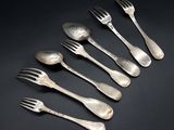 six silver spoons and a fork on a black surface