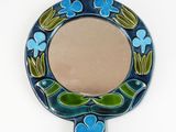 blue and green mirror with flowers and leaves on it on a white surface