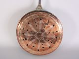 an old copper frying pan hanging on a wall