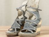 grey wedged sandal sandals on a wooden surface with a curtain in the background