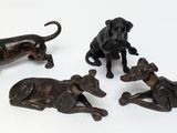 three bronze figurines of dogs and a cat on a white surface