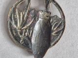 a silver pendant with a bird on it on a white surface