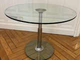 une table en verre avec un piètement en métal posée sur un parquet