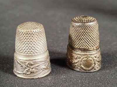 une paire de dés à coudre anciens en argent posés sur un fond noir