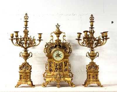 trois bougeoirs dorés et une horloge posés sur une étagère