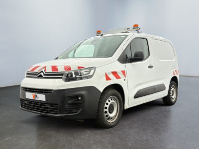La camionnette blanche est garée dans une grande pièce ; elle porte une bande rouge et blanche sur le côté.