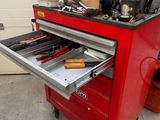 une boîte à outils rouge posée dans un garage, avec des outils dessus