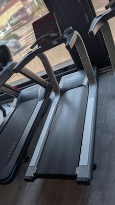 two tread machines in a gym room with a view out the window