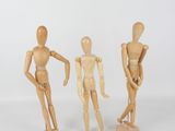 three wooden mannequins standing next to each other on a white surface