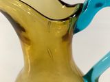 a yellow glass pitcher with a blue handle on a table