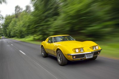 a yellow car driving down the road with trees in the background