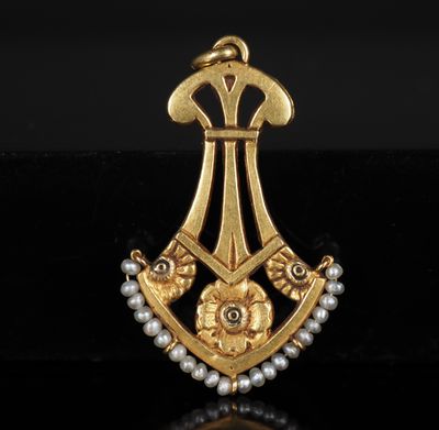 un gros plan d'une broche en or et perles posée sur une surface noire
