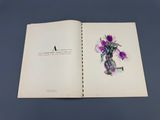 un livre ouvert sur lequel figure un dessin représentant des fleurs dans un vase posé sur une table