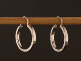 une paire de boucles d'oreilles créoles en argent fixées sur un bâtonnet en bois